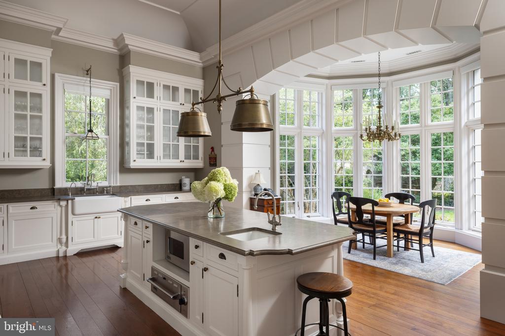 Kitchen with a large stone island and adjoining dining area surrounded by tall windows.