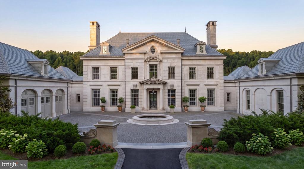 Stone mansion with slate roof, connected wings, and a circular fountain in the front courtyard.