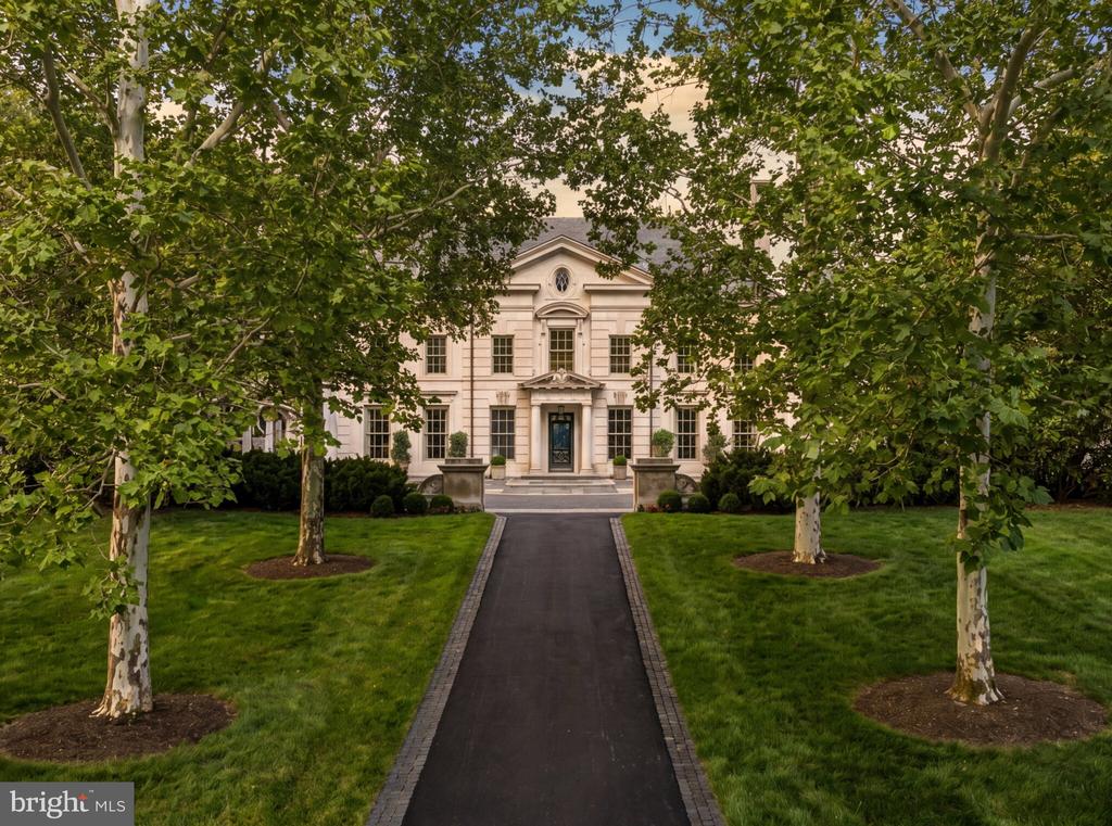 Pale-stone estate framed by leafy trees at the end of a straight driveway.