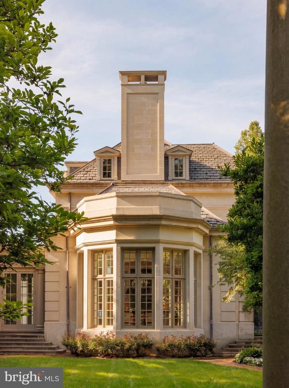 Pale stone residence with a tall chimney and a projecting bay of multipane windows.