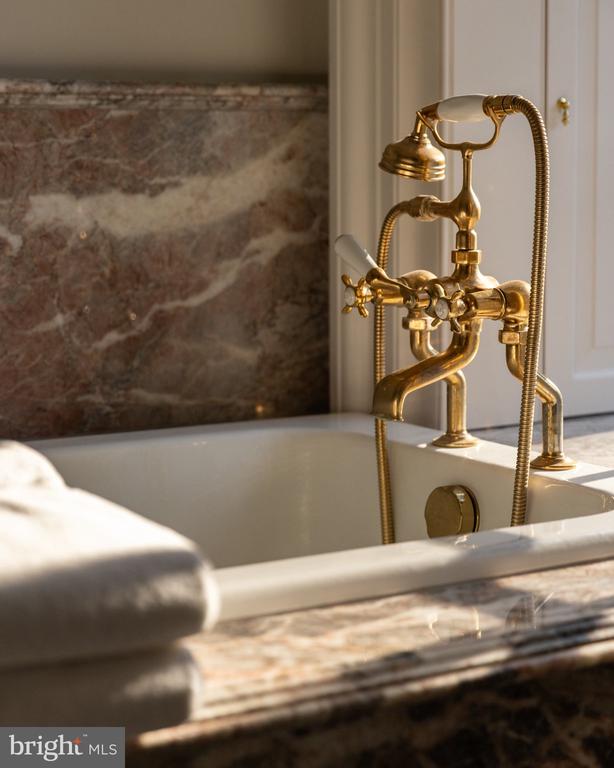 Bathtub with polished brass fixtures, marble surround, and a folded white towel.