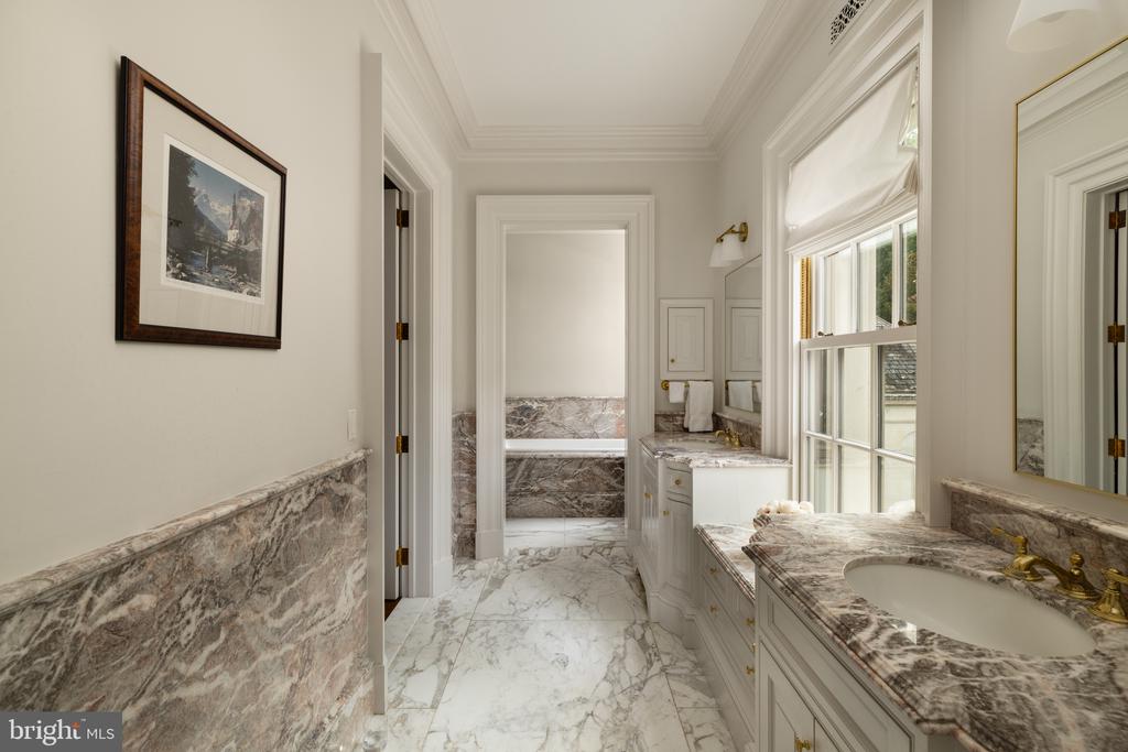 Bathroom with marble floors and countertops, white cabinetry, and a large window.