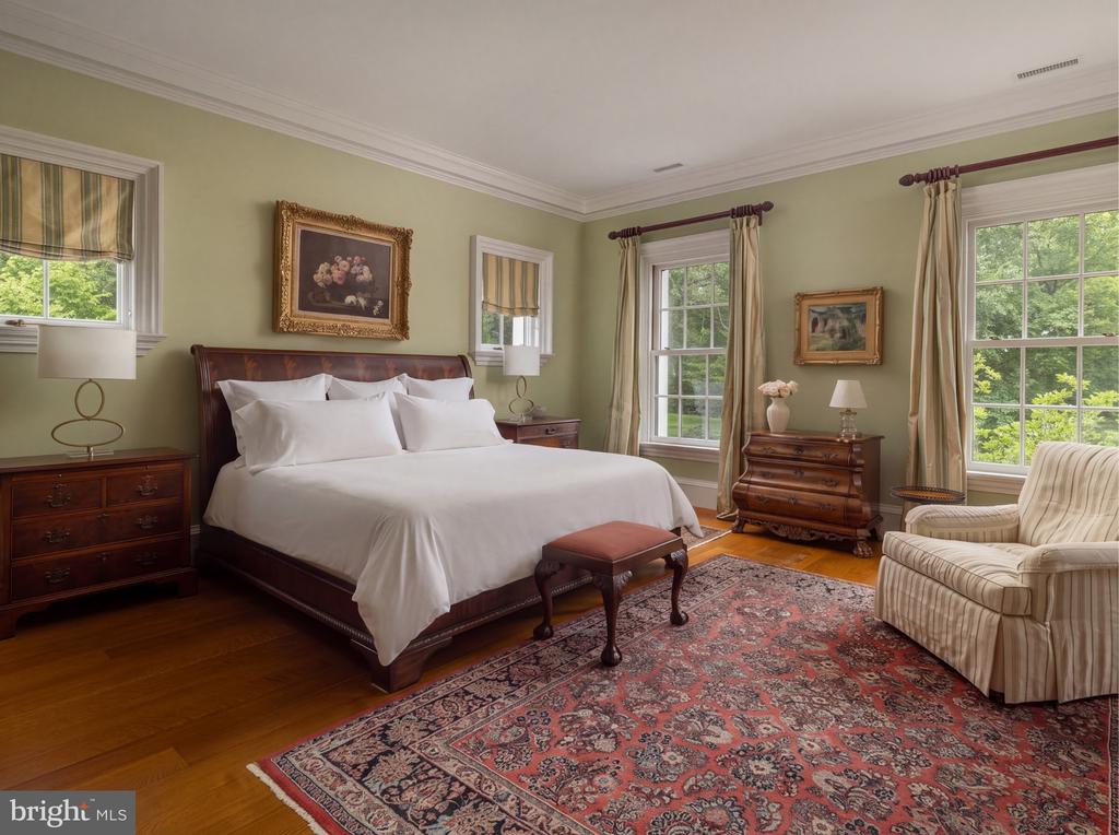 Bedroom with white bedding, sage-green walls, dark wood furniture, and windows overlooking trees.
