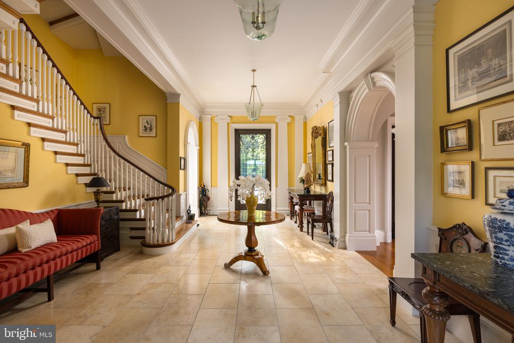 Foyer with a sweeping staircase, mustard-yellow walls, pale tile floors, and a flower-topped table.