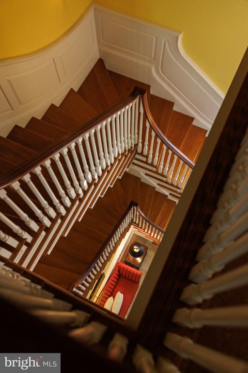Multi-level wooden staircase with white balusters and a view of a red sofa below.