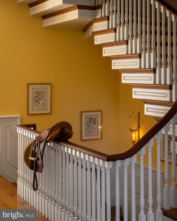Interior staircase with white balusters, dark wood railings, and a saddle resting on the landing railing.