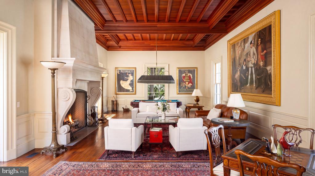 Living room with a carved stone fireplace, paneled wood ceiling, white seating, and a pool table.