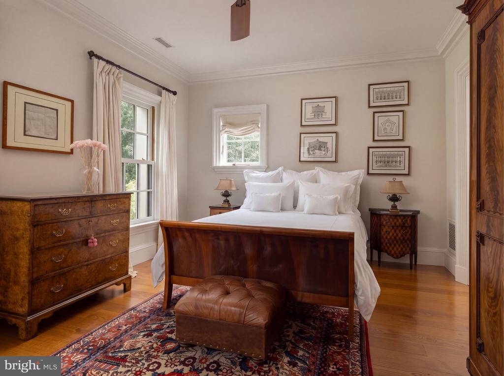 Bedroom with a dark wood bed, white linens, matching furniture, and a colorful patterned rug.