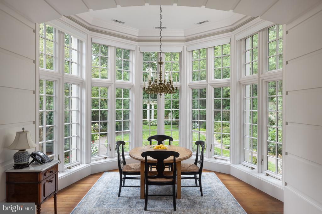 Dining room with a round table, chandelier, and tall windows overlooking a garden.