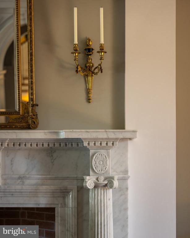 Marble fireplace with carved columns, a gold candle sconce, and the edge of a gilded mirror.
