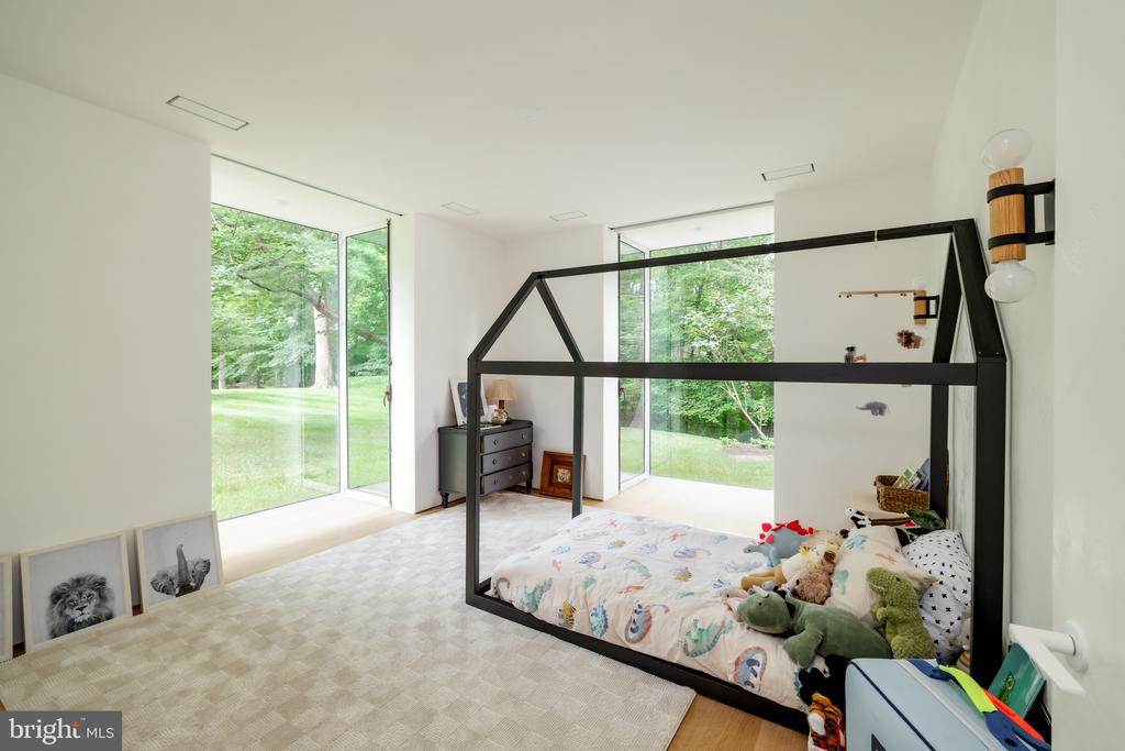 Bedroom with a black house-frame bed, plush toys, and large windows overlooking a green lawn.