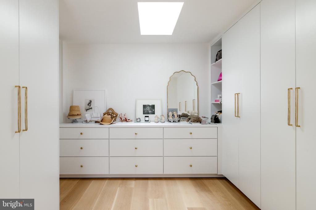 Walk-in dressing room with white built-in wardrobes, gold handles, and a scalloped mirror.