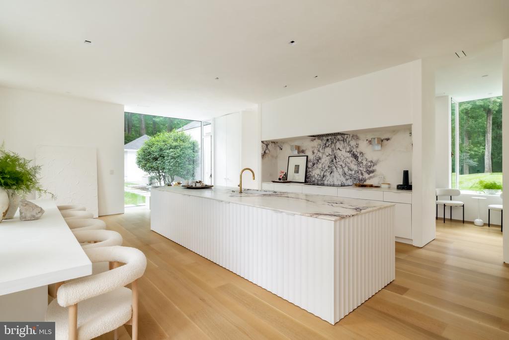 Modern kitchen with a fluted white island, marble surfaces, and windows overlooking trees.