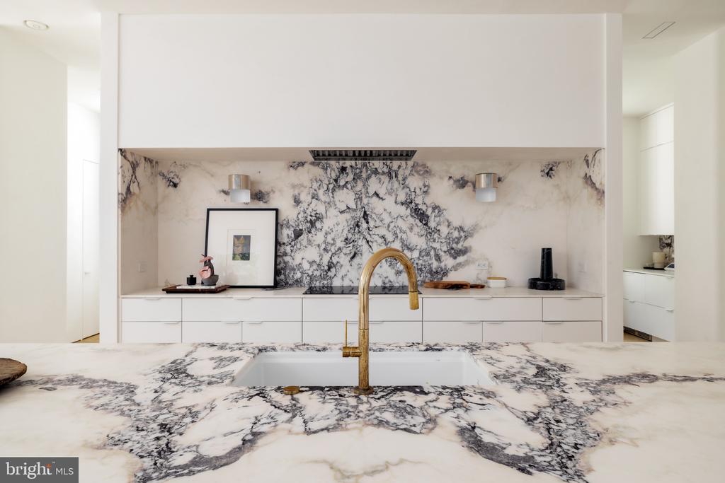 Modern kitchen with dramatic veined marble counters and backsplash, white cabinetry, and a gold faucet.