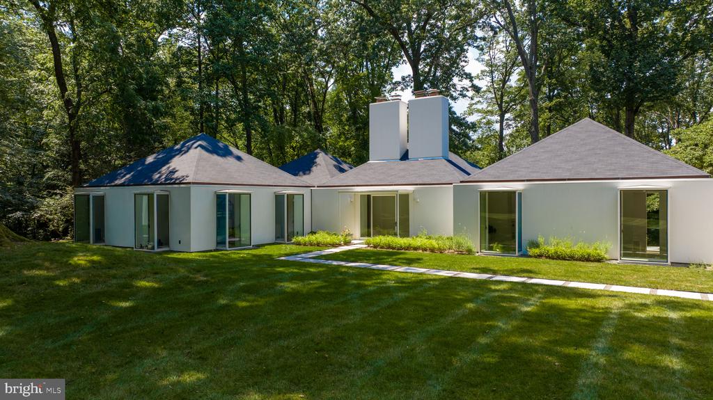Modern white single-story house with large windows, a broad lawn, and mature trees.