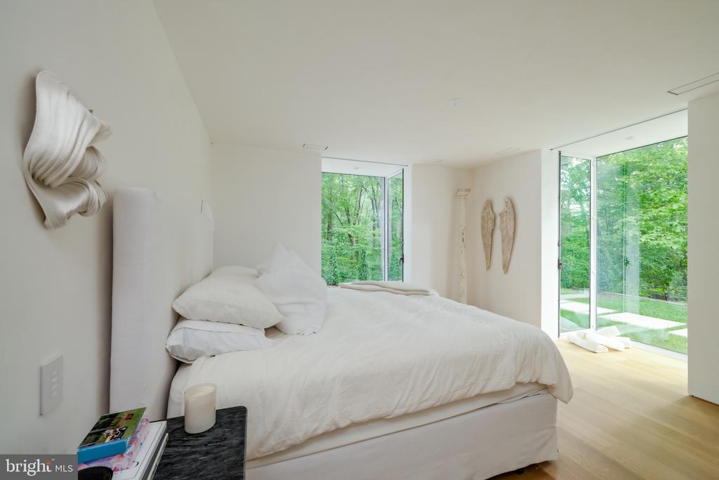 Bedroom with a white bed and floor-to-ceiling windows overlooking trees and lawn