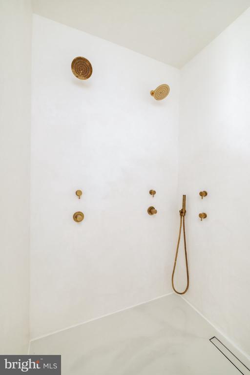 Minimalist white shower with brass fixtures, handheld wand, and linear floor drain.