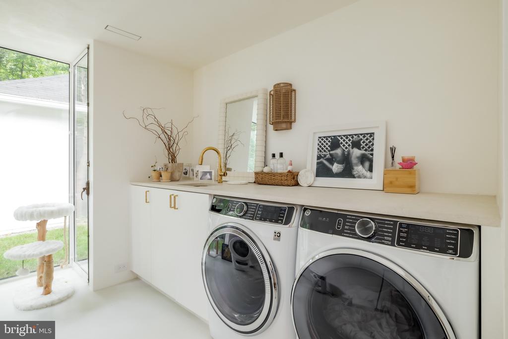 Laundry room with front-loading washer and dryer beneath a counter, beside a glass door to the yard.