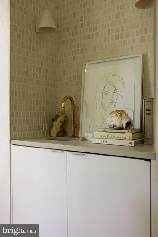 Bathroom vanity with a gold-tone faucet, tiled walls, framed line art, and books on the counter.