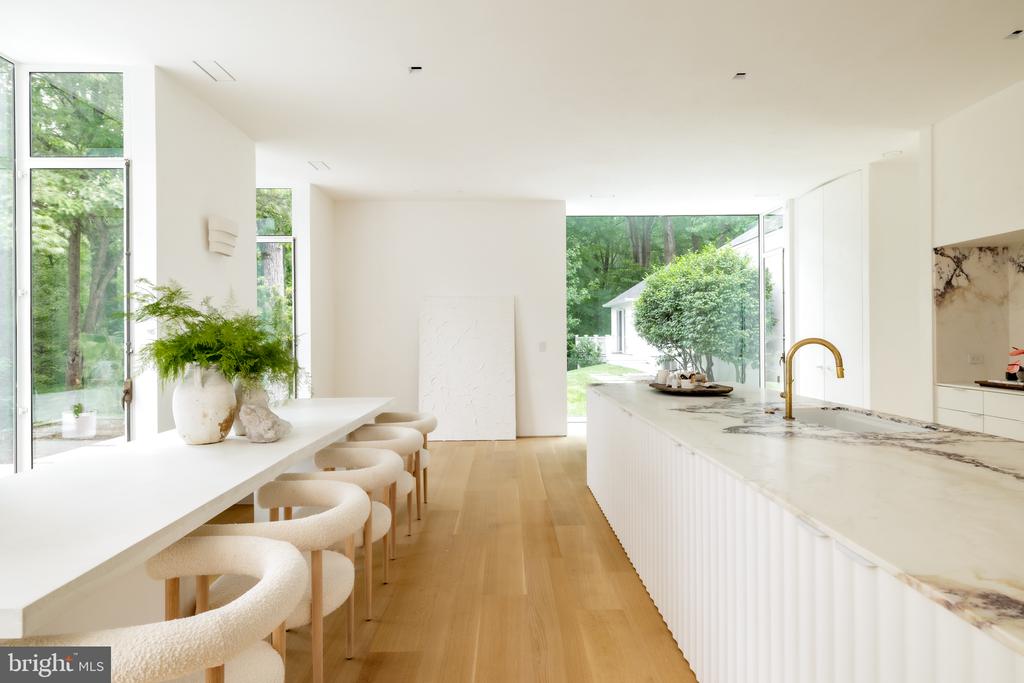 Contemporary kitchen with a long marble island, brass faucet, and large garden-facing windows.