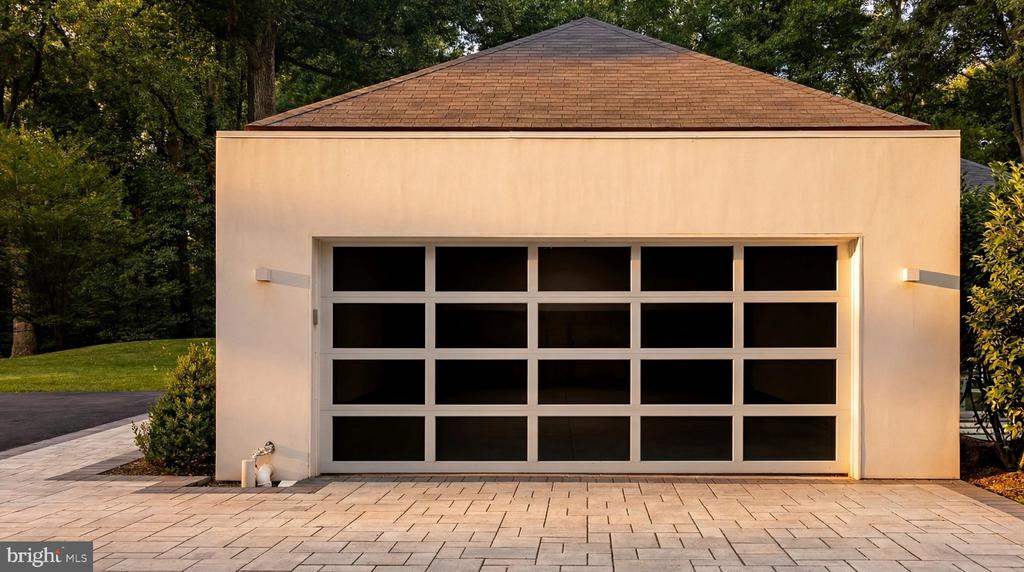 Detached garage with a wide glass-panel door, pale stucco facade, and paved driveway.