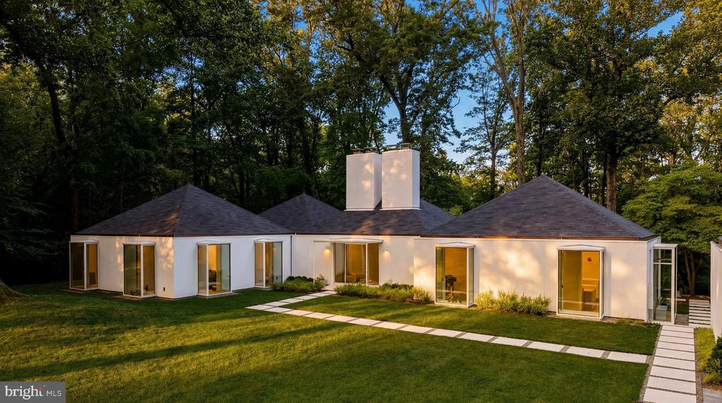 Modern white home with glass doors, a curved walkway across the lawn, and mature trees.