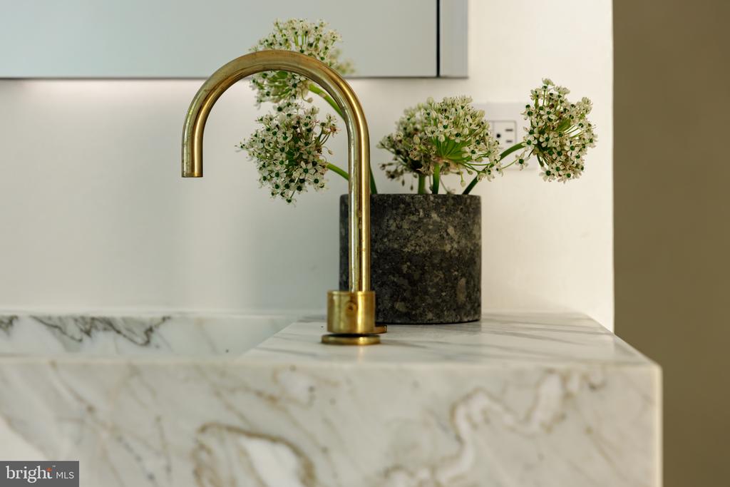 Bathroom vanity with a brass faucet, veined marble countertop, and white flowers.