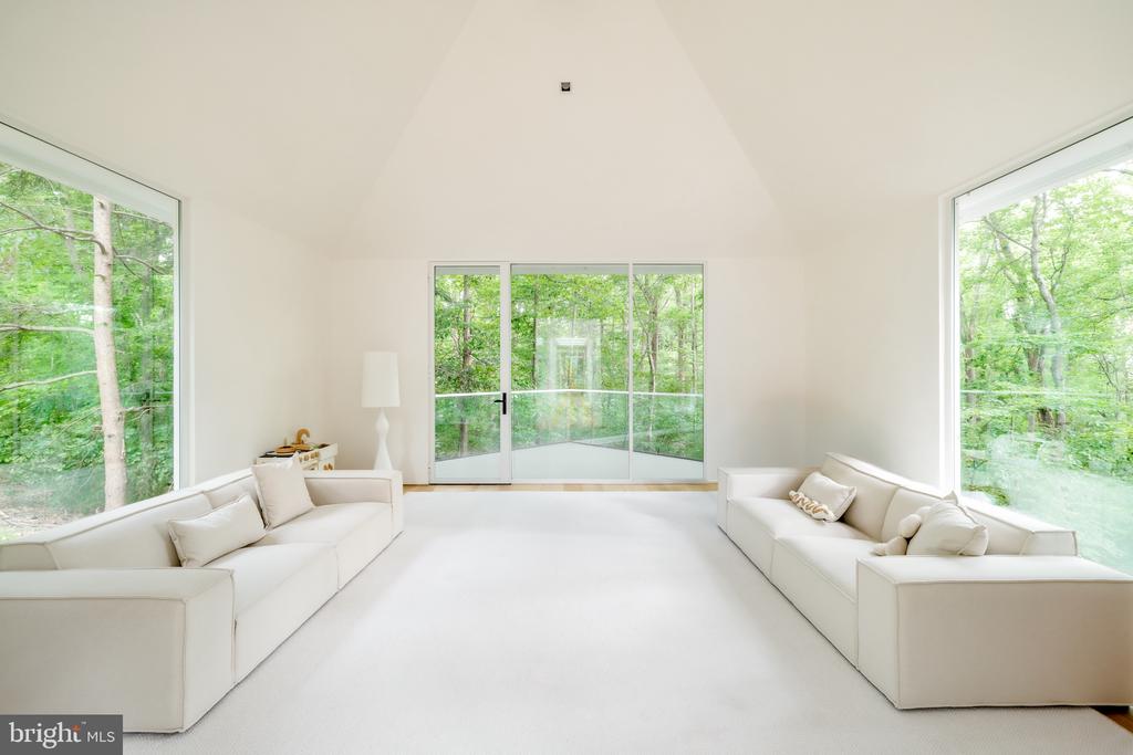 Living room with white sofas, a vaulted ceiling, and large windows overlooking woodland.