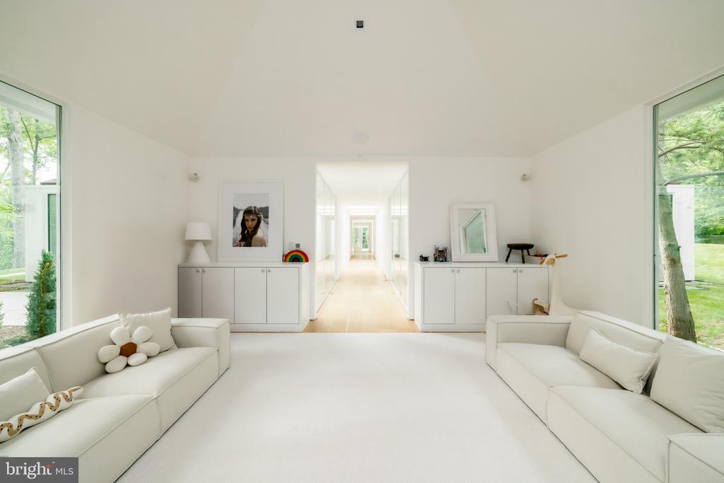 Bright white living room with facing sofas and a long hallway between glass doors.