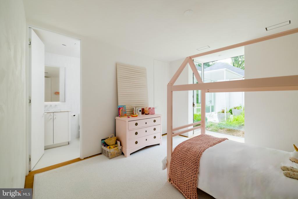 Bedroom with a pink canopy bed and dresser, opening onto a garden through glass doors.