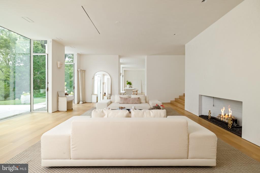 Contemporary living room with white sofas, expansive windows, pale wood floors, and a linear fireplace.