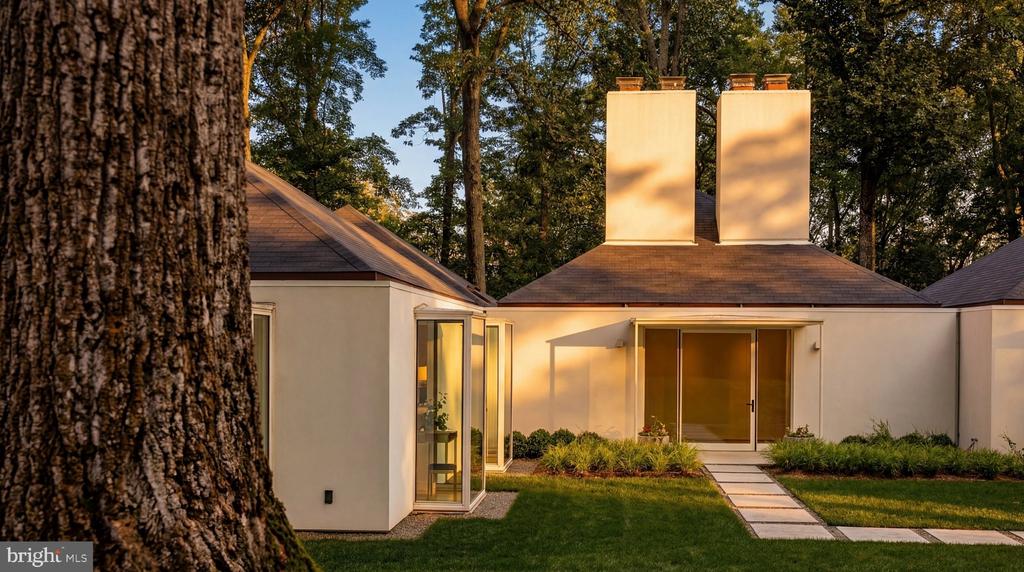 Modern white home with twin chimneys, a glass-sided room, and a stepping-stone path through the lawn.