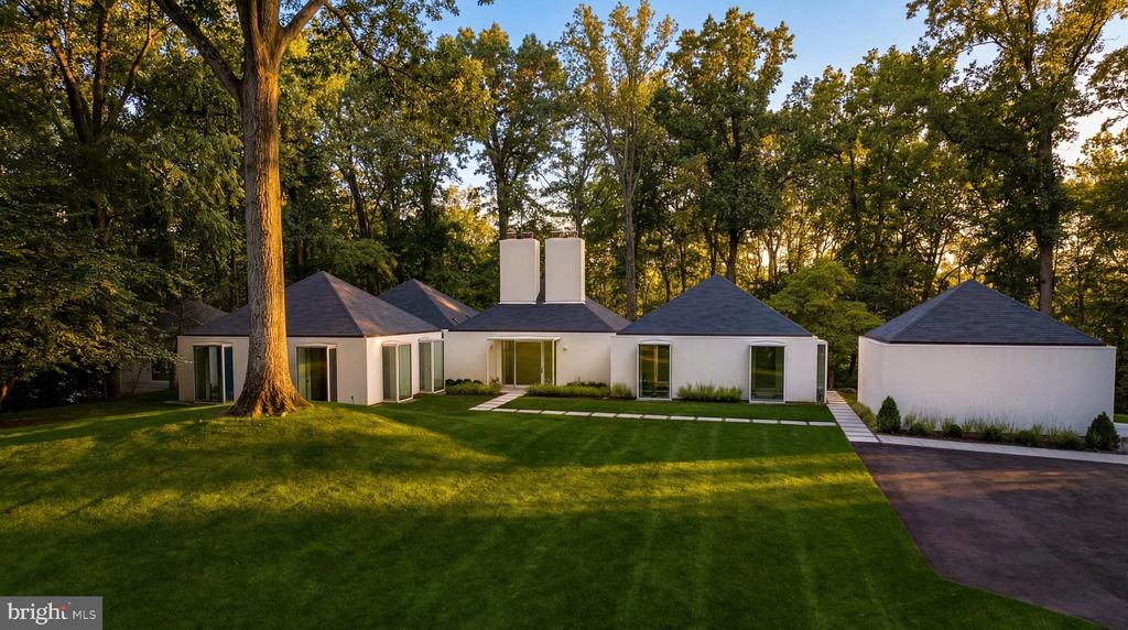 Modern white home and detached garage surrounded by a broad lawn and mature trees.