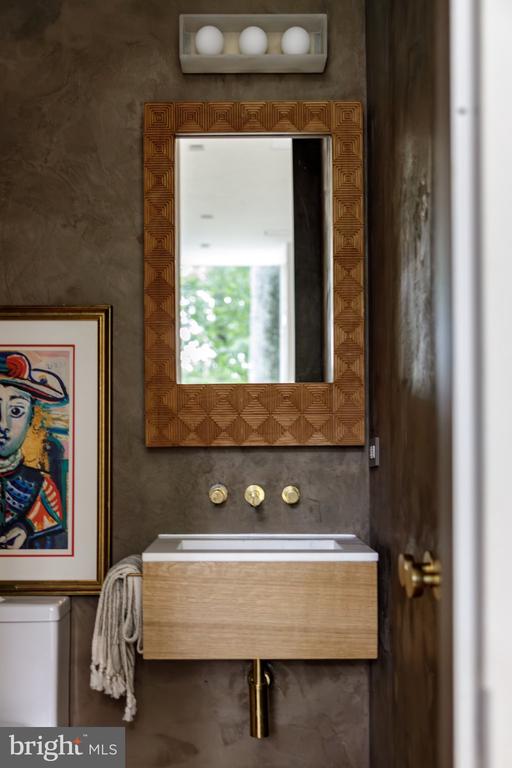Powder room with a floating wood vanity, geometric mirror, and colorful framed artwork.