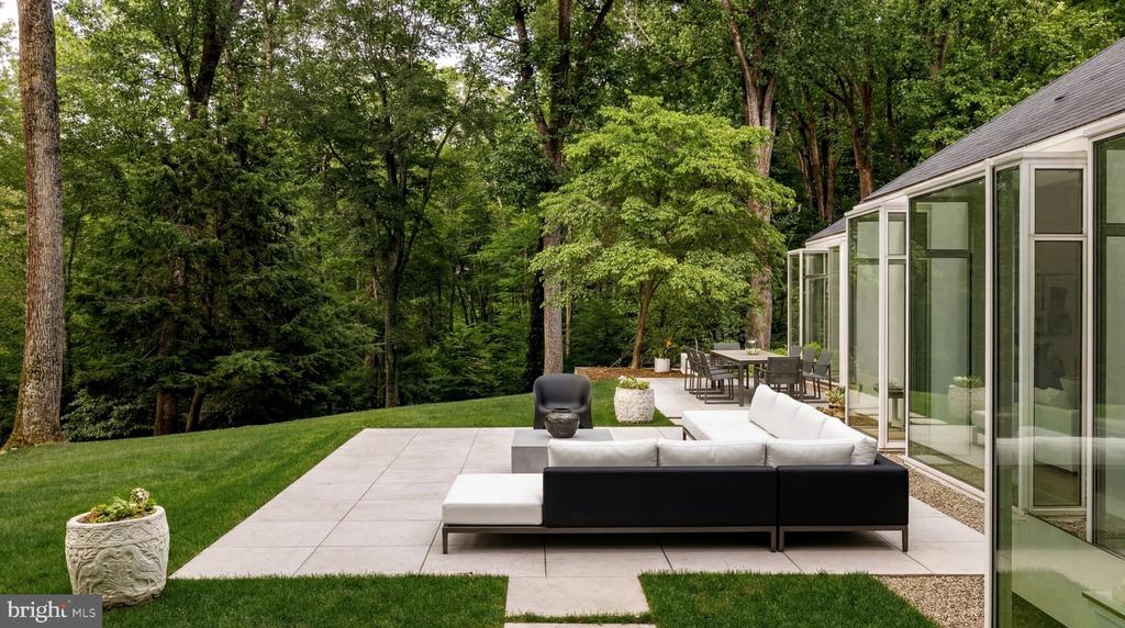 Modern home patio with sectional seating and dining table beside a wooded lawn.