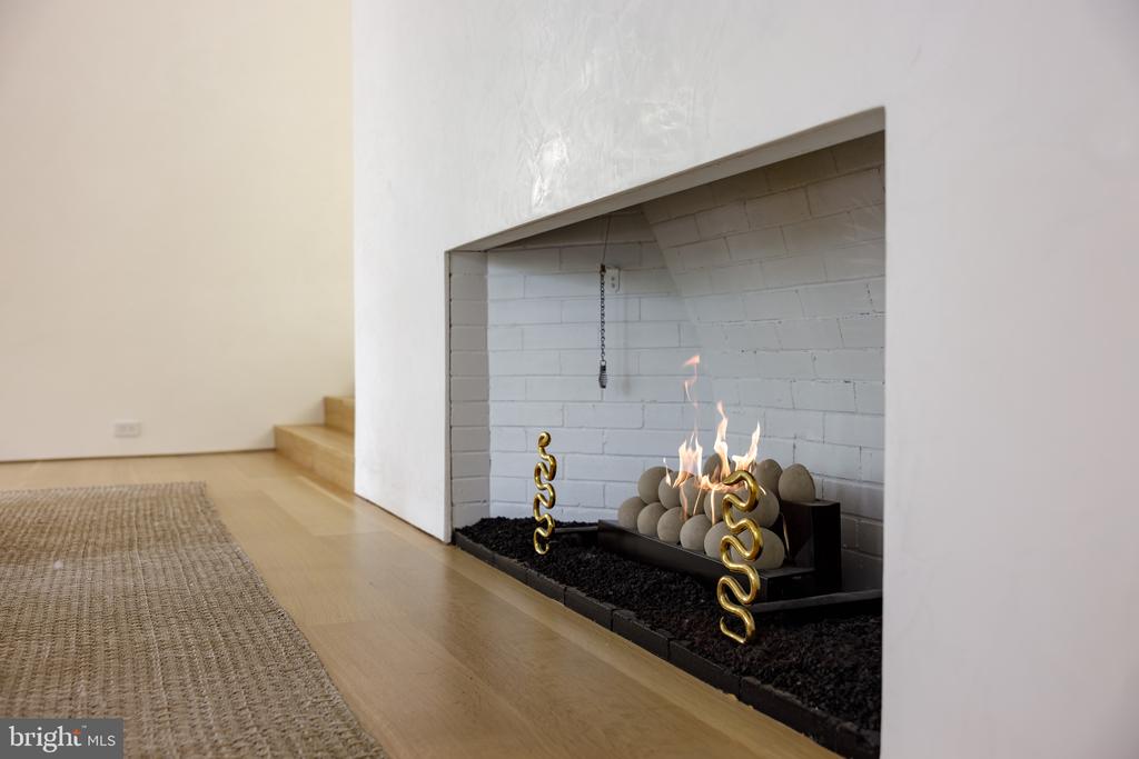 Modern fireplace with gas flames, white brick surround, and brass fireplace tools.
