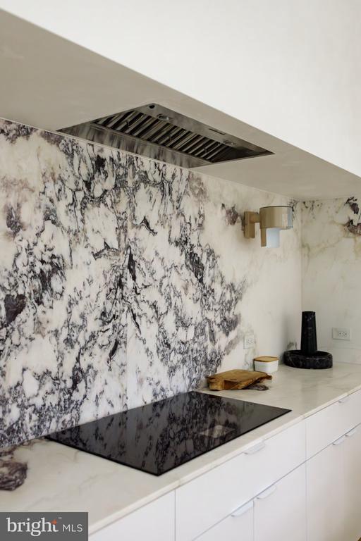 Kitchen with a black induction cooktop, dramatic veined stone backsplash, and white cabinetry.