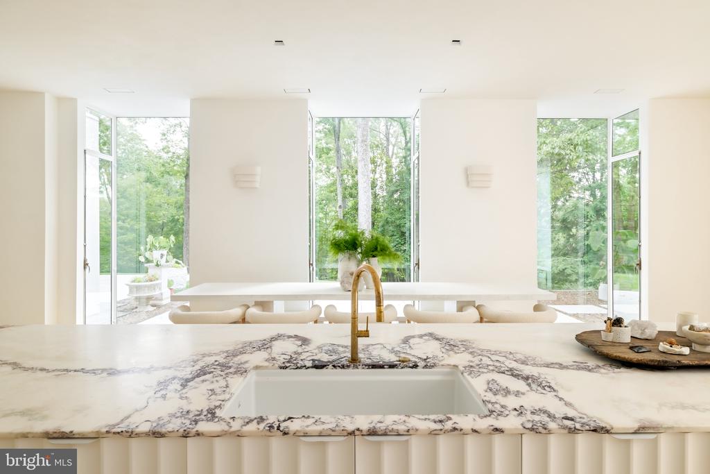 Modern kitchen with a veined marble island, brass faucet, and windows overlooking greenery.