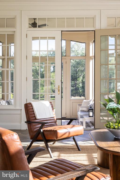 Sunlit living room with brown leather lounge chairs and tall divided-light windows overlooking greenery.