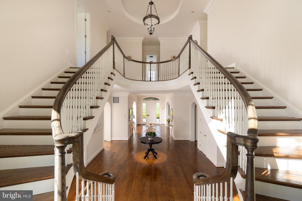 Two-story foyer with a curved split staircase, dark wood handrails, white balusters, and polished wood floors.