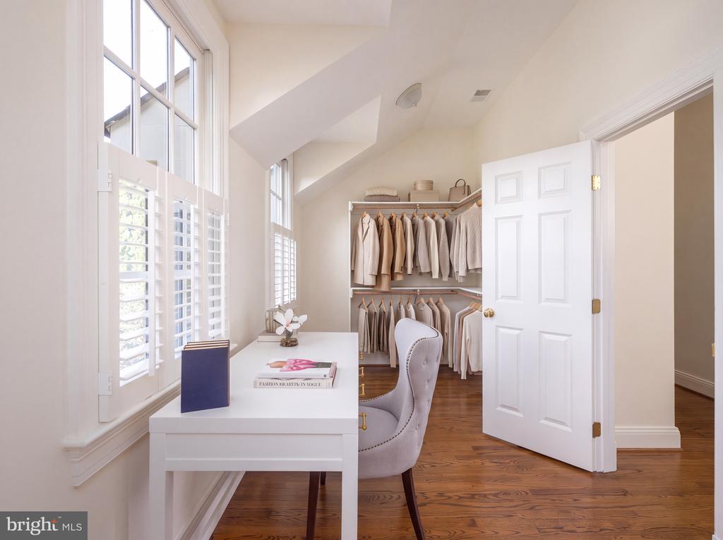 Bright dressing room with a walk-in wardrobe, desk, tall shuttered windows, and hardwood floors.