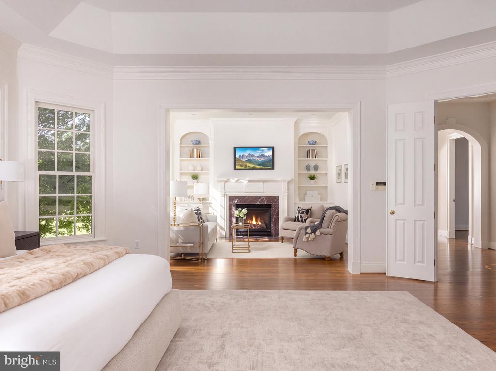 Living room with a large window and hardwood floors, opening onto a fireplace sitting area.