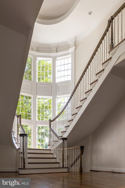 Two-story entry hall with a sweeping staircase and tall windows overlooking greenery.