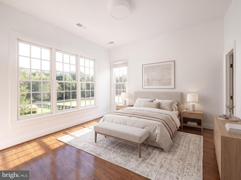 Bright bedroom with a neutral bed and bench beside large windows overlooking a green lawn.