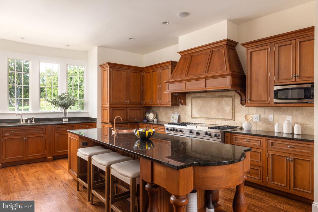 Kitchen with cherry cabinetry, a large dark-stone island, and a prominent wood range hood.