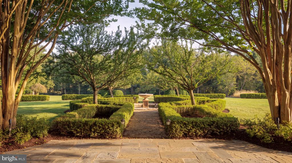 Formal garden with clipped hedges, a stone path, central fountain, and mature trees.