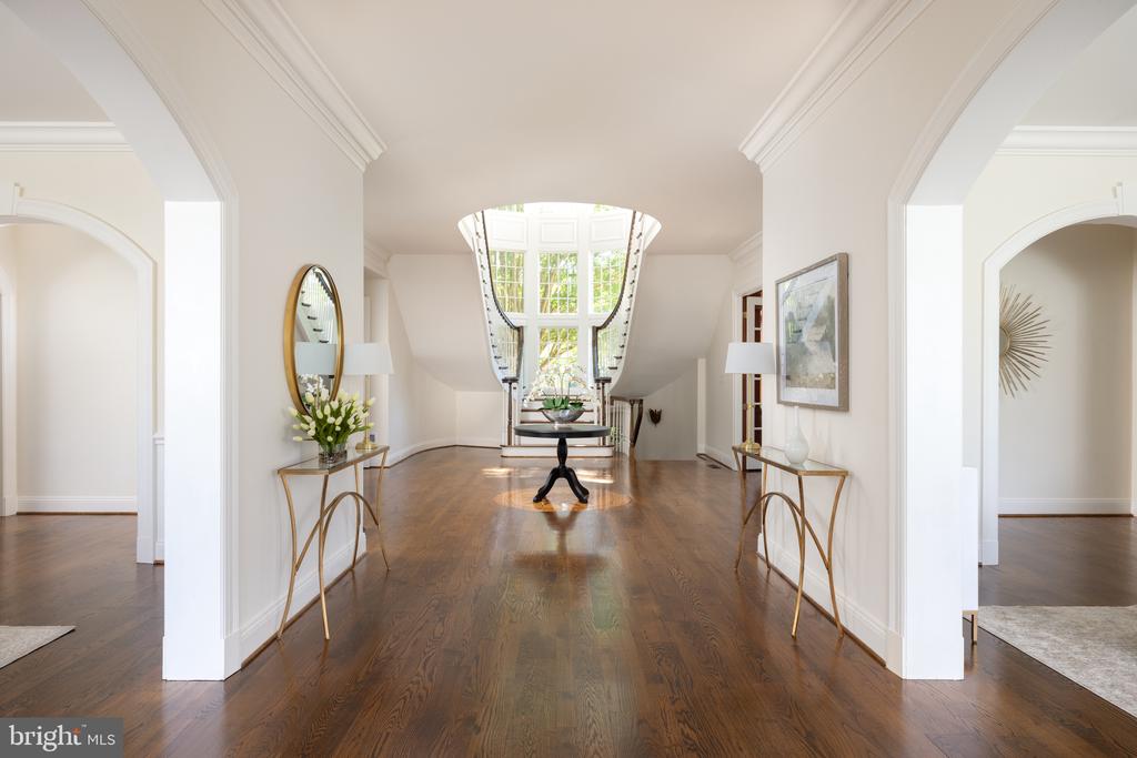 Furnished foyer with hardwood floors, console tables, and a staircase beneath a large arched window.