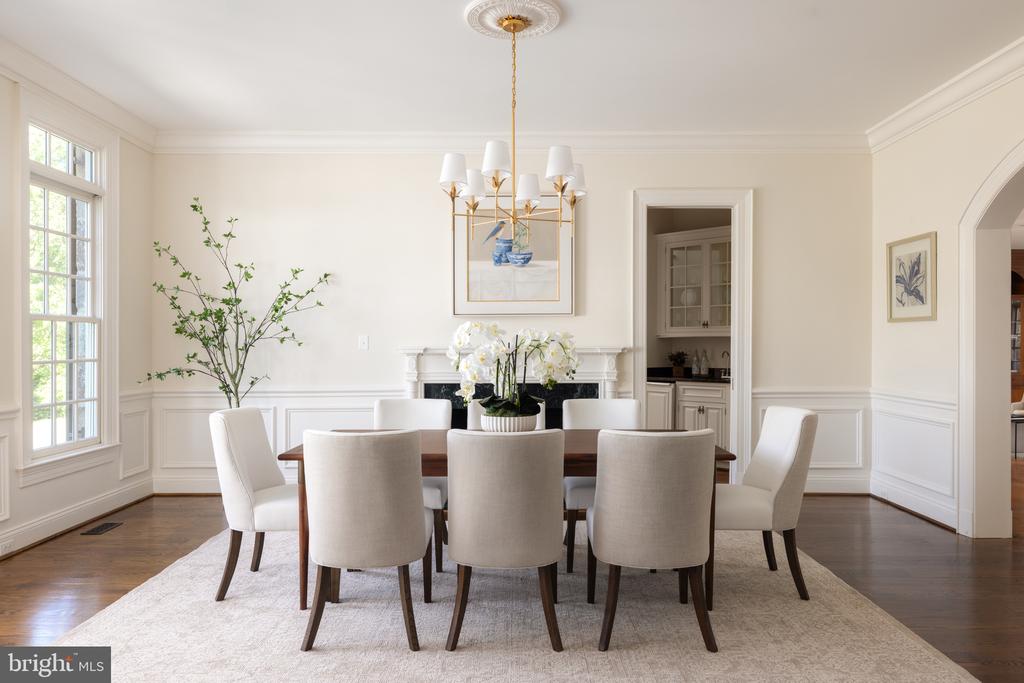 Formal dining room with upholstered chairs, brass chandelier, fireplace, and tall windows.