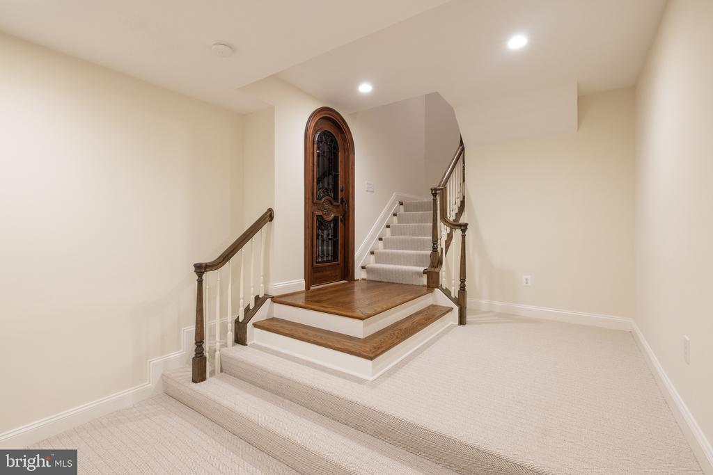 Stair hall with a raised wood landing, arched wooden door, and carpeted staircase with dark railings.