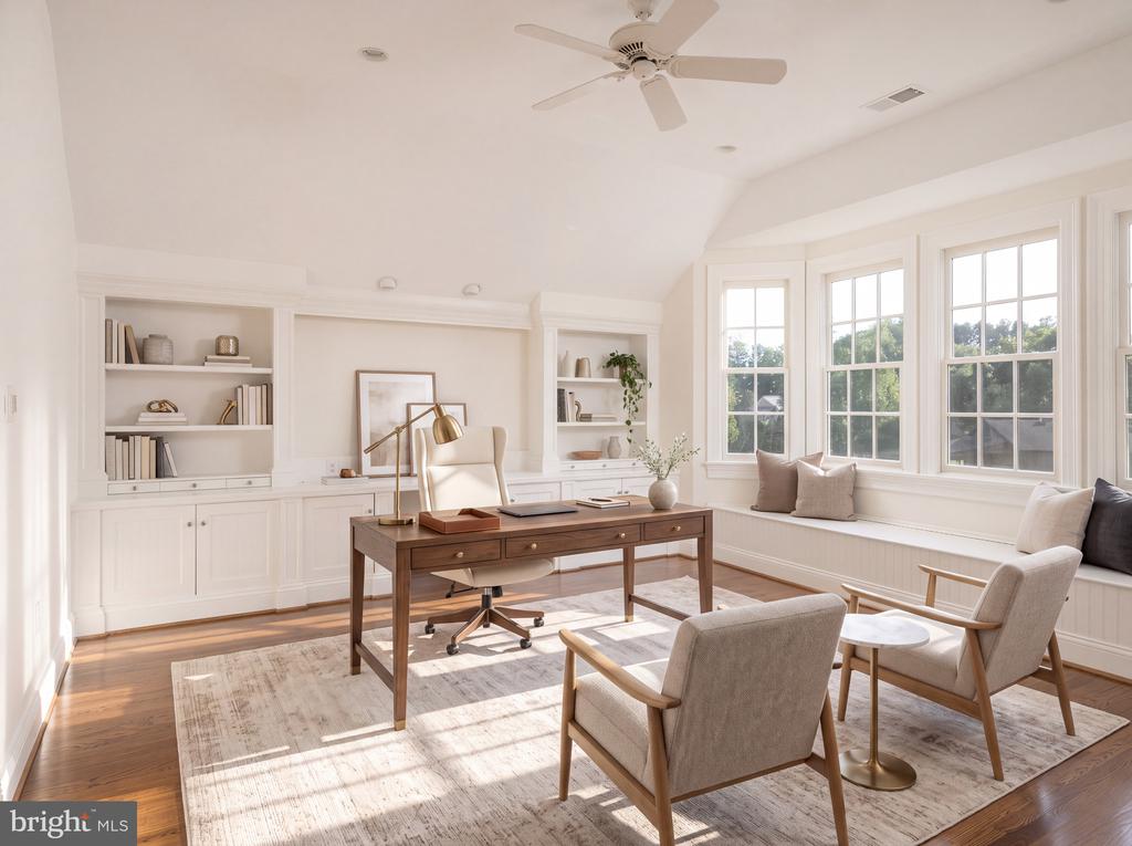 Staged home office with built-in bookshelves, a wood desk, and large sunny windows.